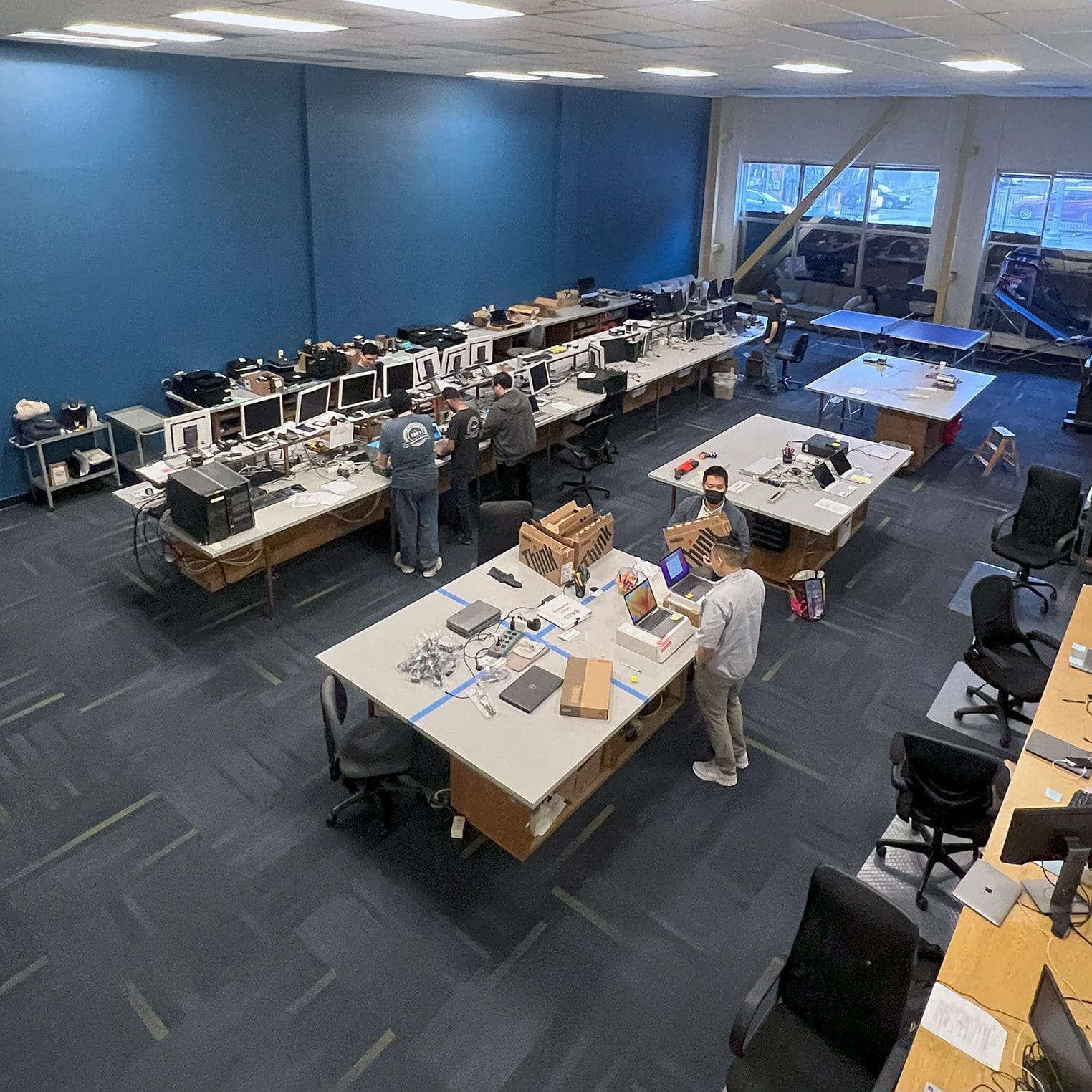 Overhead view of an IT assembly lab with technicians at multiple workstations.